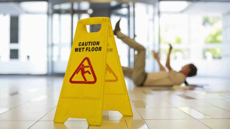 caution plate for wet and slippery floor and a person slip and fell on floor in background.