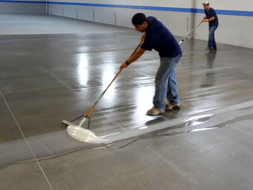 two persons applying coating on the concrete floor with mop.
