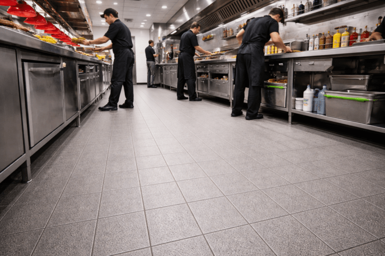 Busy fast-food commercial kitchen with chefs working during service, viewed from a low angle highlighting a clean, textured anti-slip floor designed for kitchen safety and hygiene